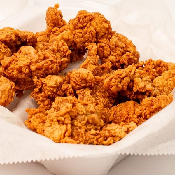 Crispy fried chicken pieces in a white takeout container lined with parchment paper.
