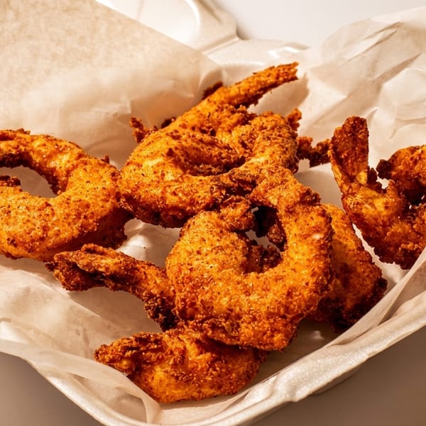 Crispy fried shrimp in a white takeout container lined with parchment paper.